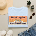 Light blue lizard graphic T-shirt with retro desert print: “Basking in Resentment”.