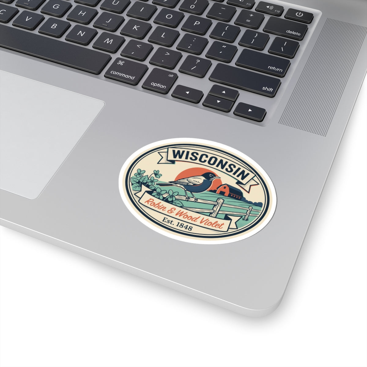 Round Wisconsin badge sticker on laptop lid; robin on fence with flowers and “Est. 1848”.