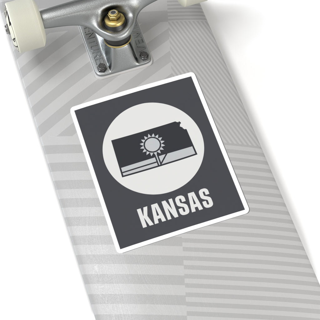 Kansas state sticker on a striped board, dark gray square with sun and wheat field
