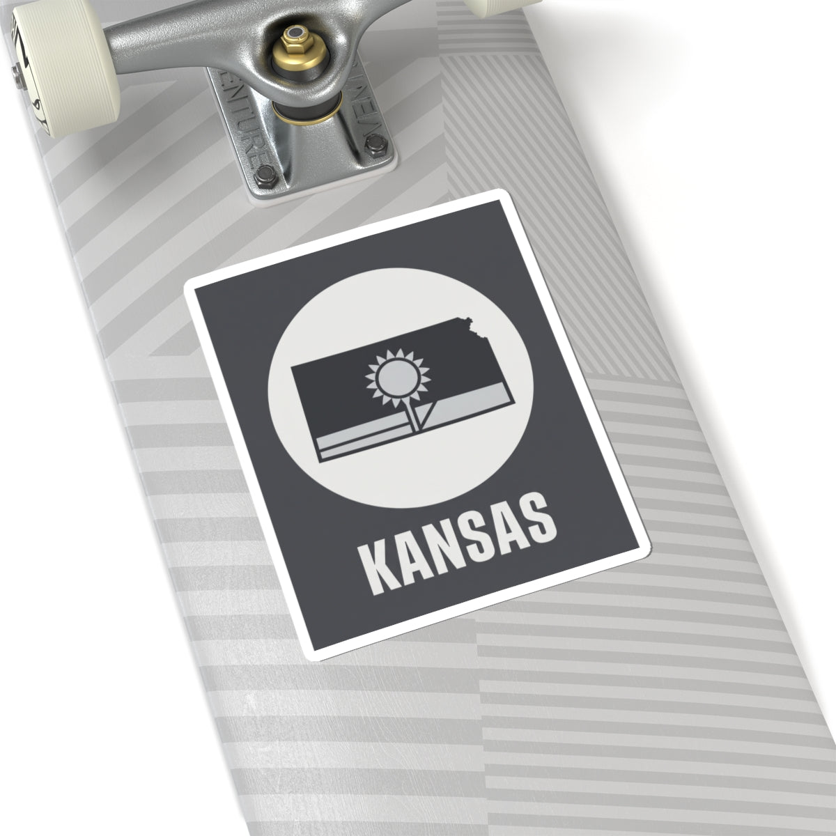 Kansas state sticker on a striped board, dark gray square with sun and wheat field