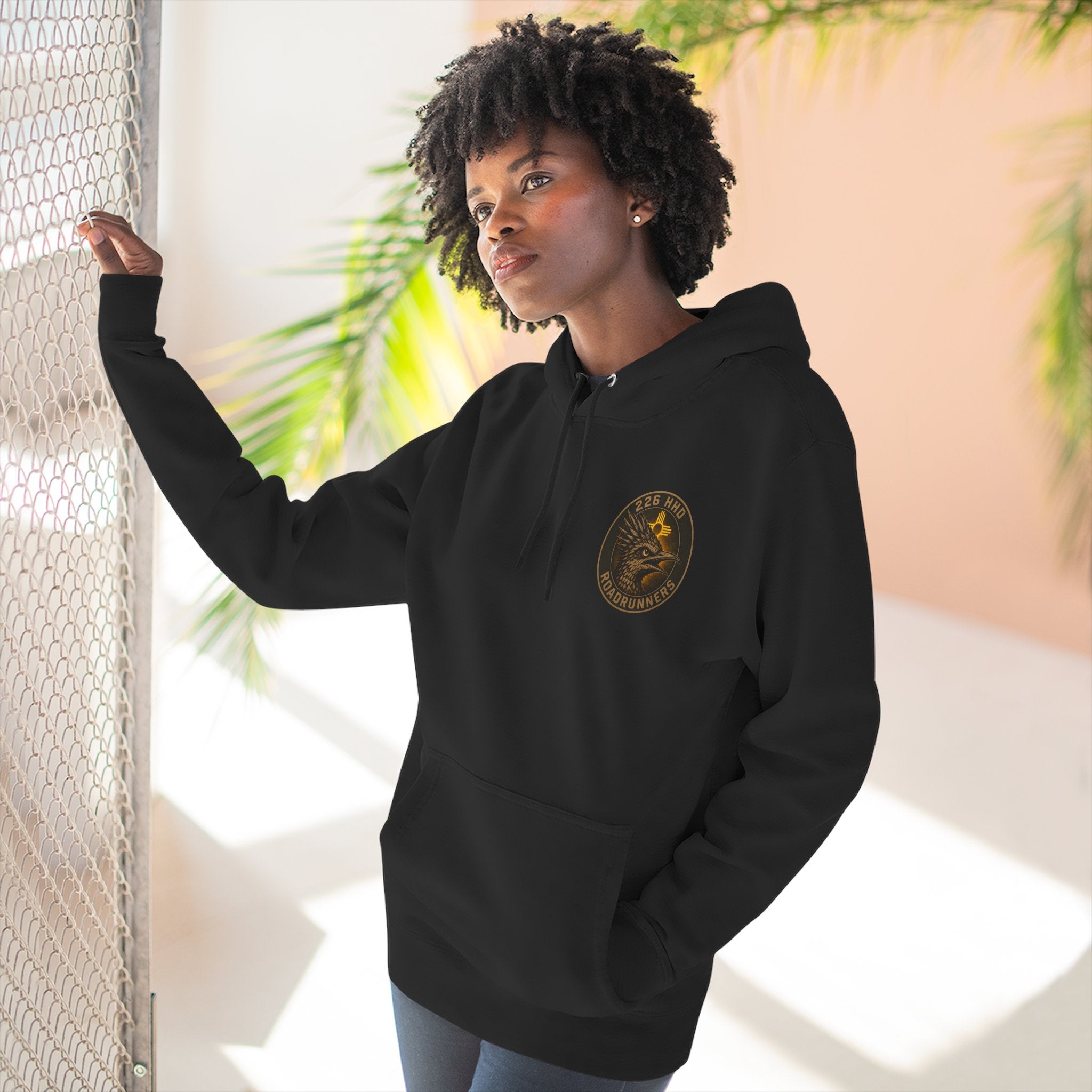 Black cotton pullover hoodie with kangaroo pocket and chest emblem, worn.