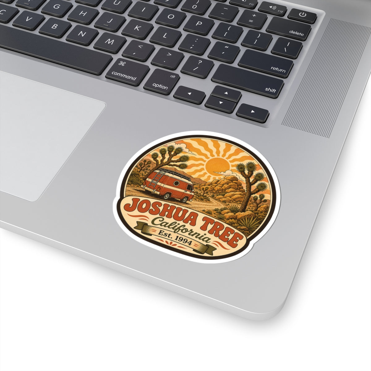Round white-edged sticker on a laptop showing desert art with retro van and Joshua Tree California Est. 1994