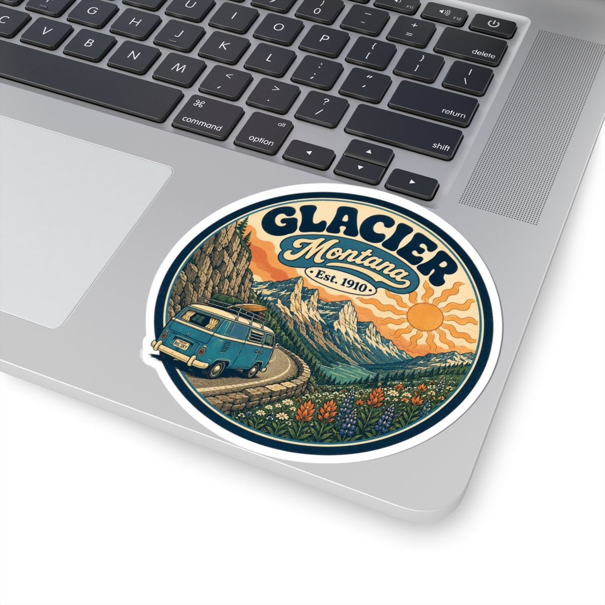 Round kiss-cut sticker with Glacier Montana emblem, teal camper van road scene, and mountain range
