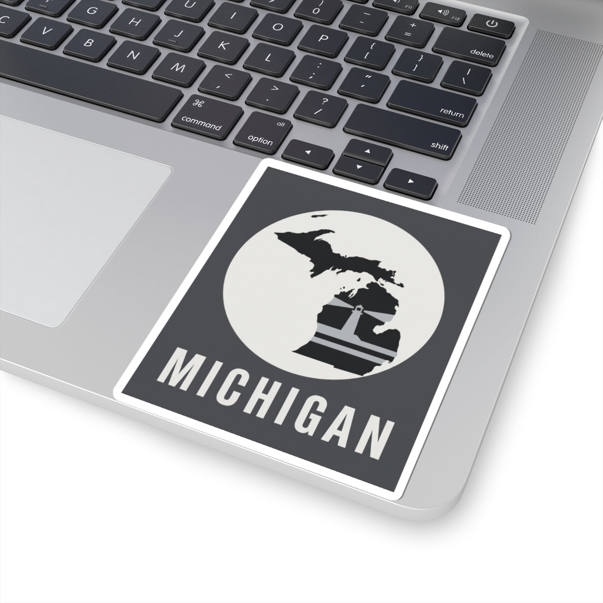 Square Michigan decal on a laptop, black silhouette with lighthouse and “MICHIGAN” word.