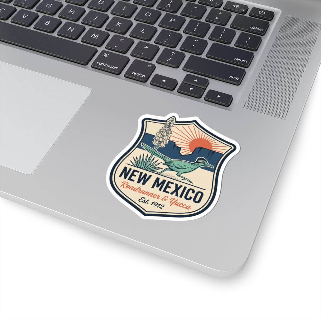 Shield-shaped New Mexico sticker on a laptop keyboard: roadrunner, yucca, badge design