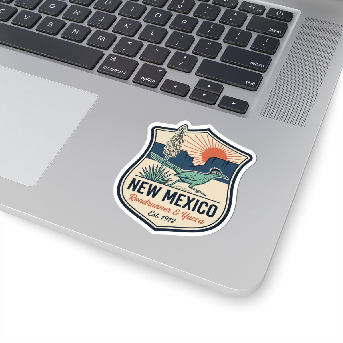 Shield-shaped New Mexico sticker on a laptop keyboard: roadrunner, yucca, badge design