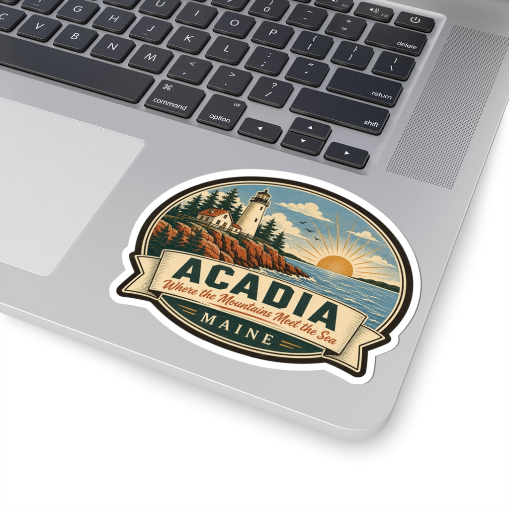 Round Acadia Maine sticker on laptop lid with lighthouse scene, sunrise, and 'Where the Mountains Meet the Sea'.