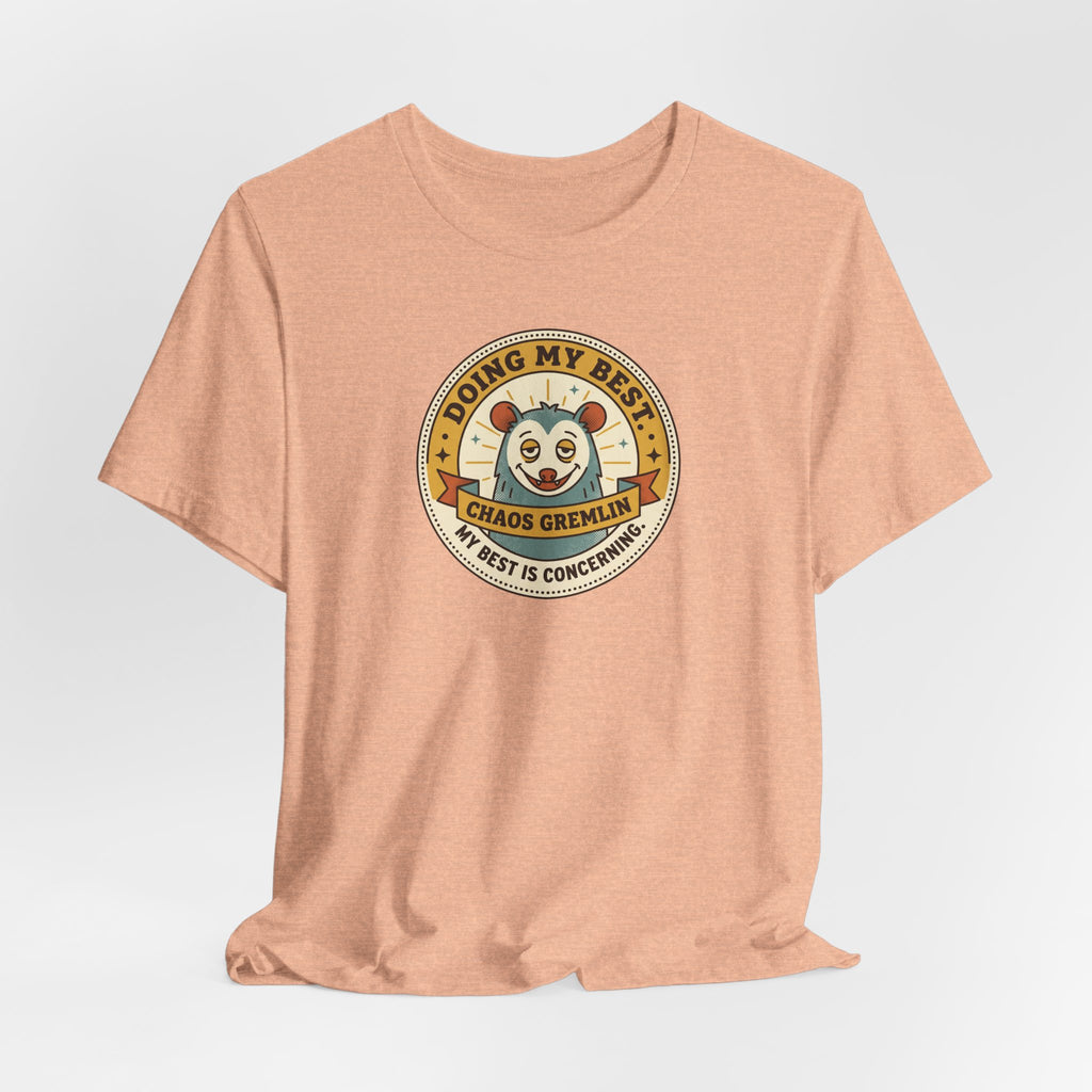 Peach crewneck T-shirt with round cartoon gremlin badge graphic centered on chest