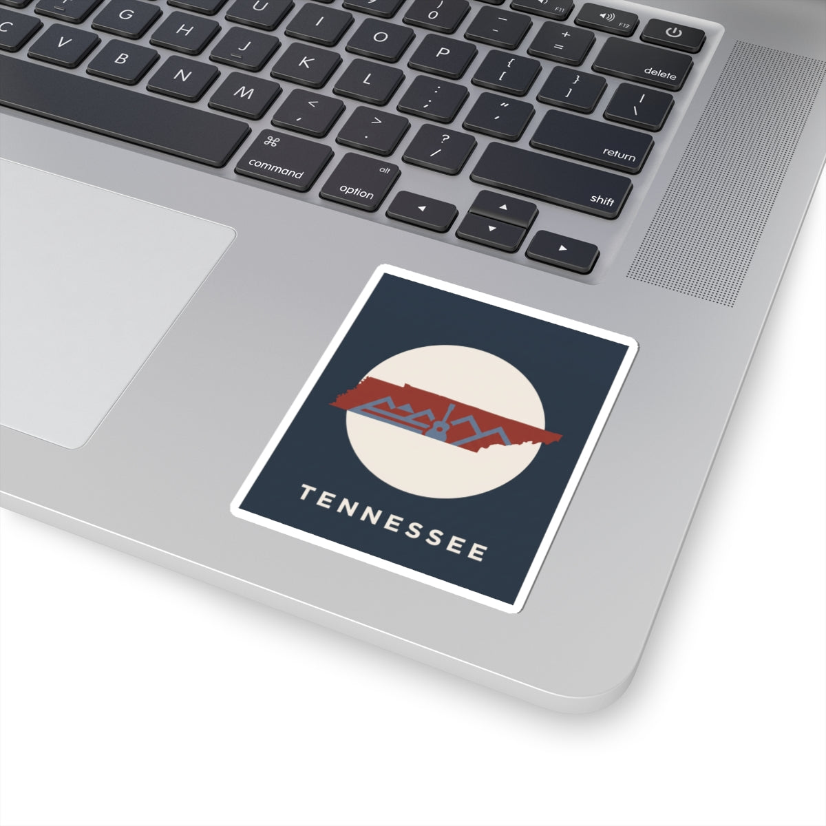 Tennessee outline sticker with retro mountains and guitar, shown on a laptop keyboard