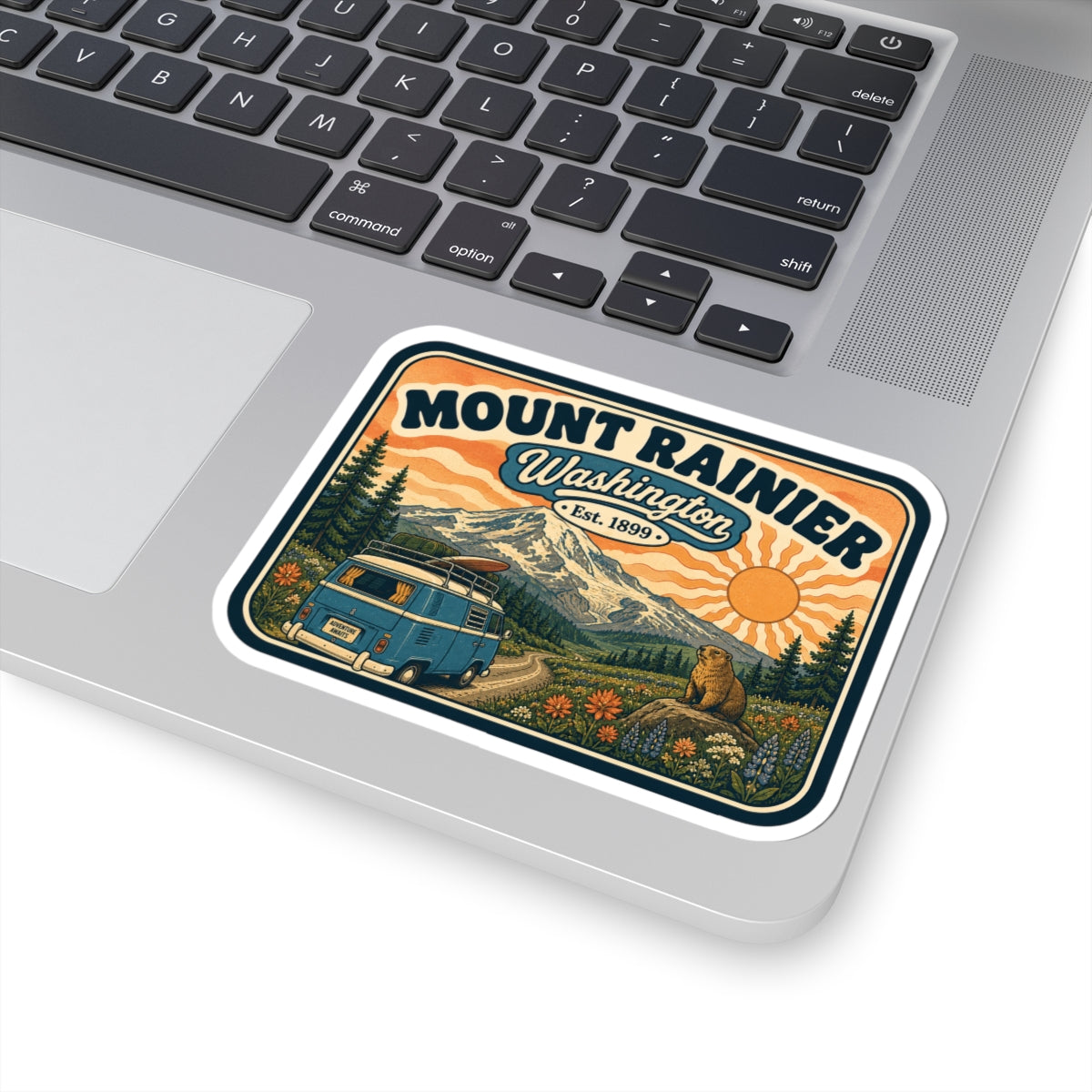 Mount Rainier sticker centered on laptop, vintage camper van, mountains, sun, and bear