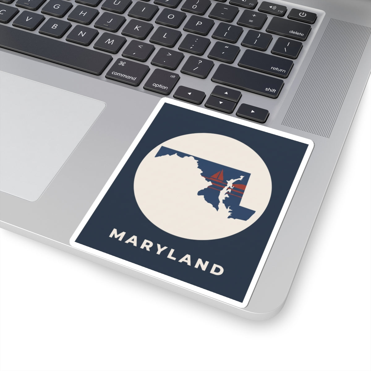 Maryland sticker on laptop surface, navy square border with sailboat and “MARYLAND”