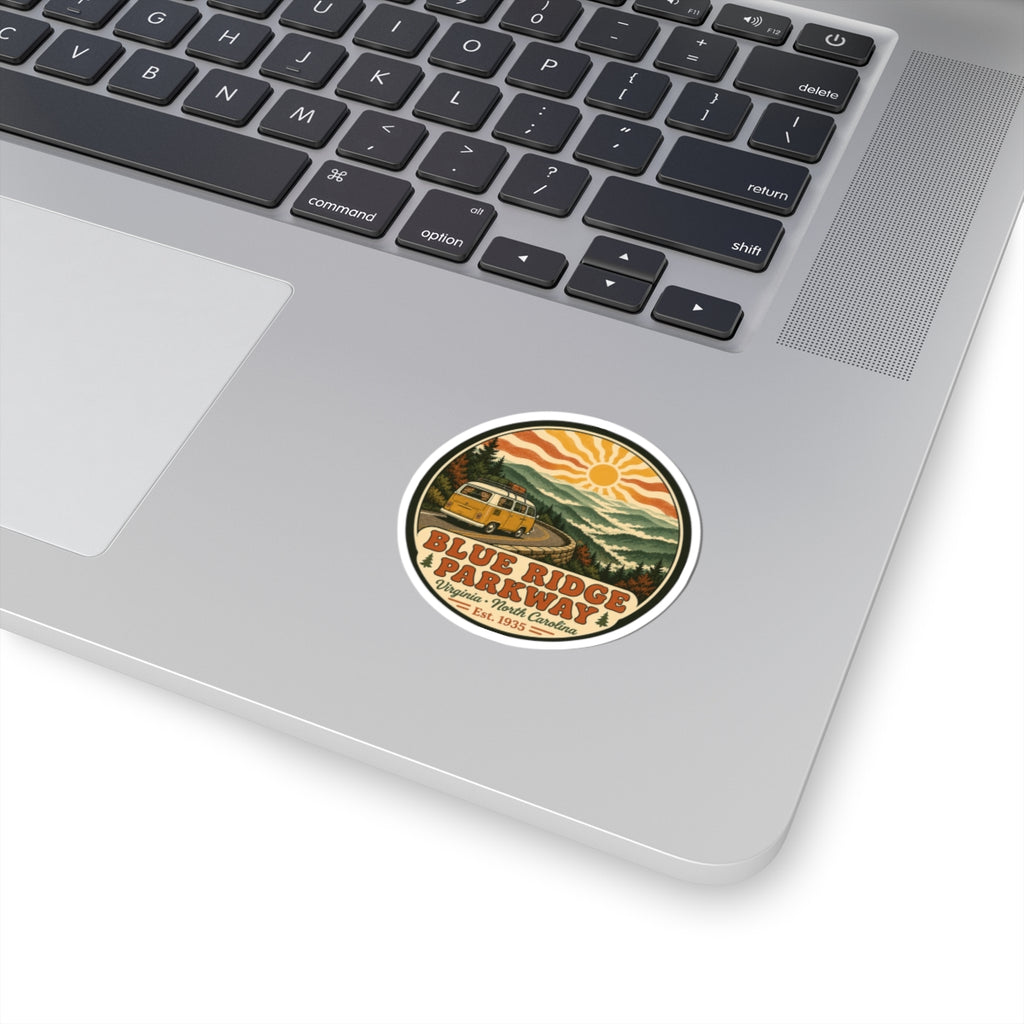Round vintage-style sticker with camper, mountains, and orange sun; white border.