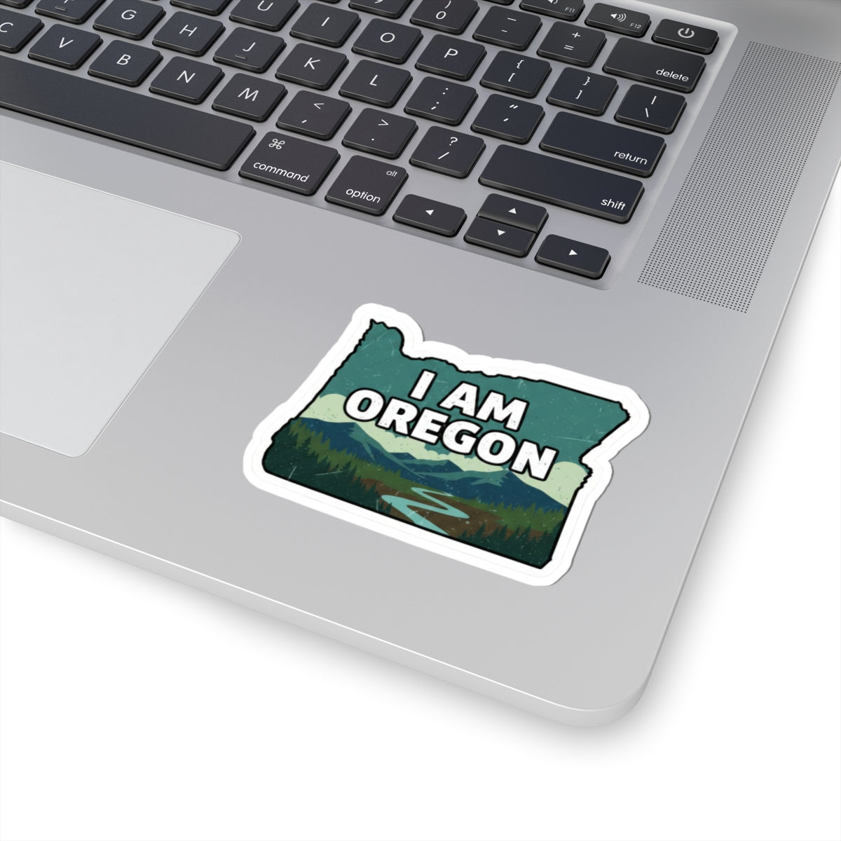 Vinyl sticker with white outline reading “I AM OREGON” over a scenic landscape