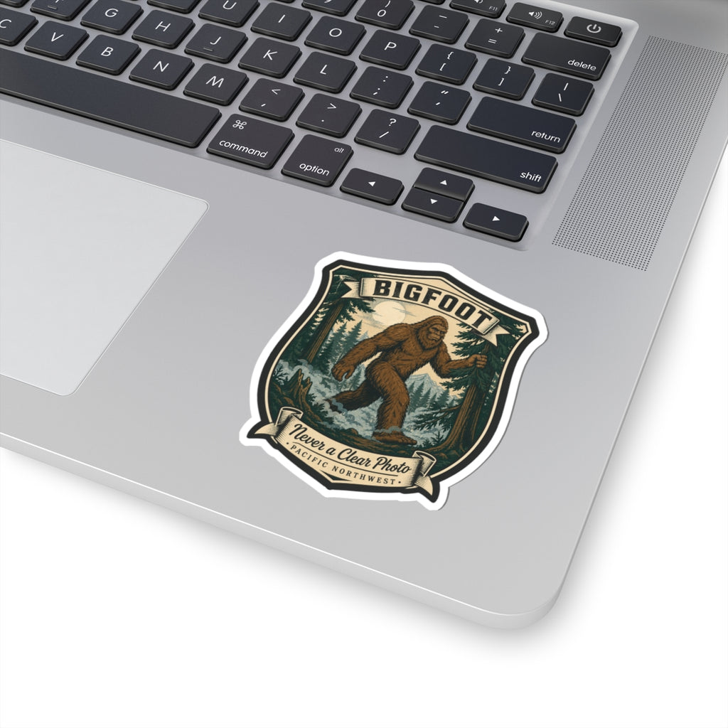 Small Bigfoot hiking badge sticker on laptop lid, brown Sasquatch forest shield artwork
