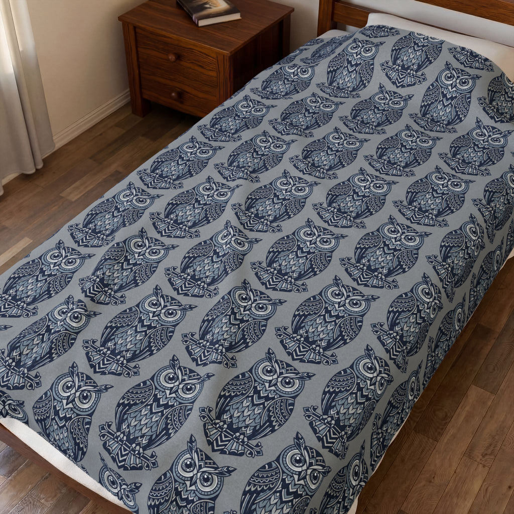 Blue owl-pattern plush blanket with repeating owl prints on bed, draped flat