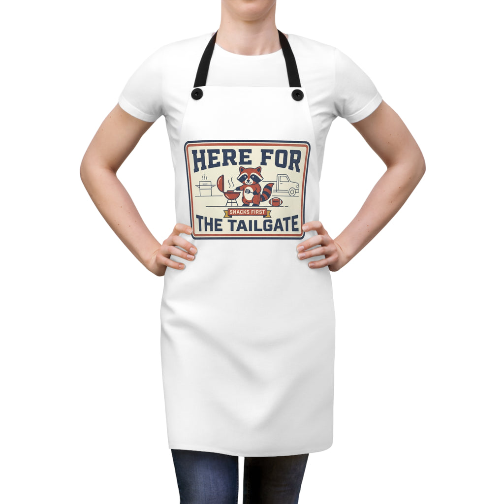 Apron on person: white BBQ apron with black straps and raccoon tailgate logo