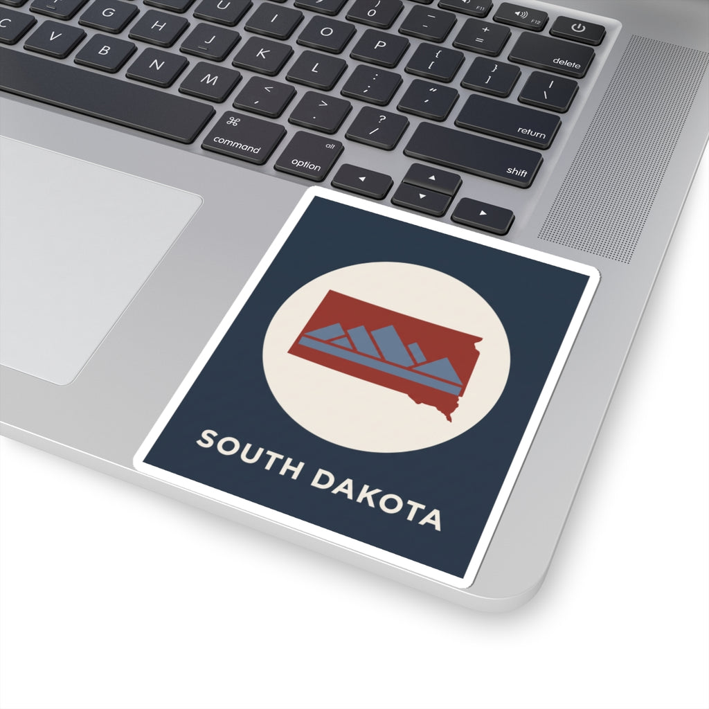 South Dakota map badge sticker on laptop keyboard, navy square with white circle and red state outline
