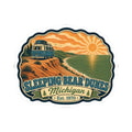 Die-cut sticker with camper van on dunes, shoreline trail, sunrise sky, and “Sleeping Bear Dunes” title
