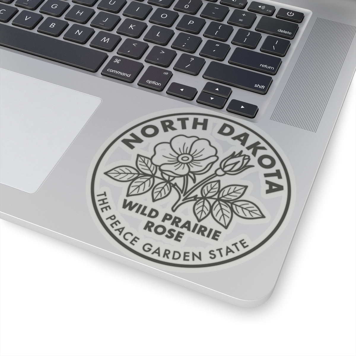Transparent vinyl sticker on laptop lid showing North Dakota wild prairie rose garden state