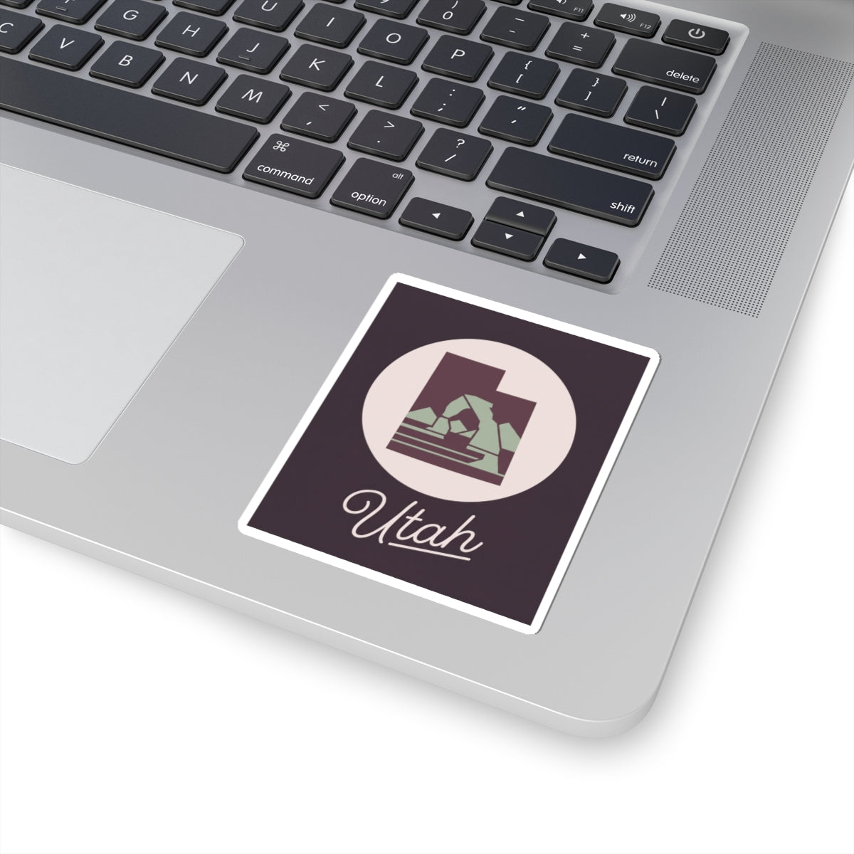 Utah state kiss-cut decal sticker on a laptop, dark purple square with circular mountain and “Utah”.