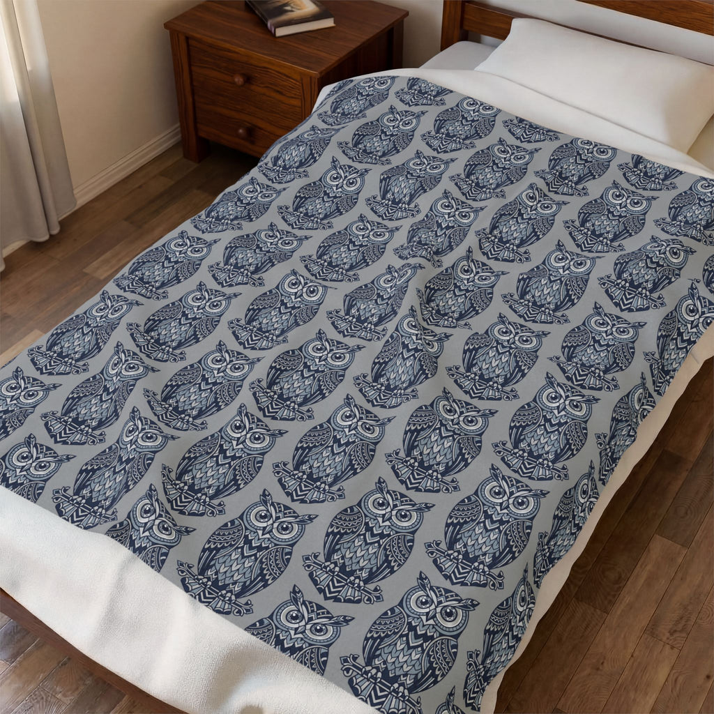 Blue owl-pattern plush blanket with repeating owl prints on bed, close view