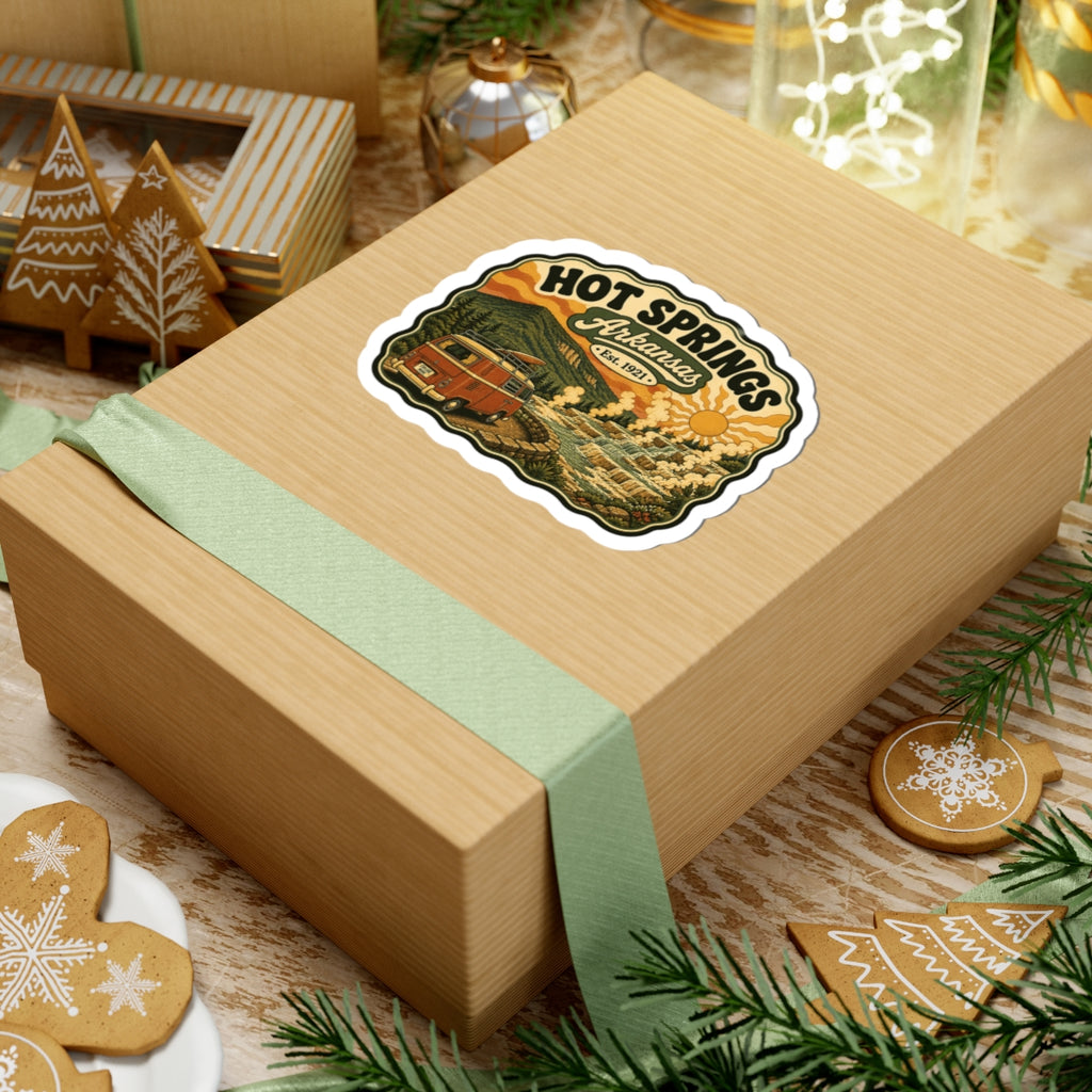 Die-cut Hot Springs Arkansas sticker on a wrapped gift box, vintage camper van and hot springs