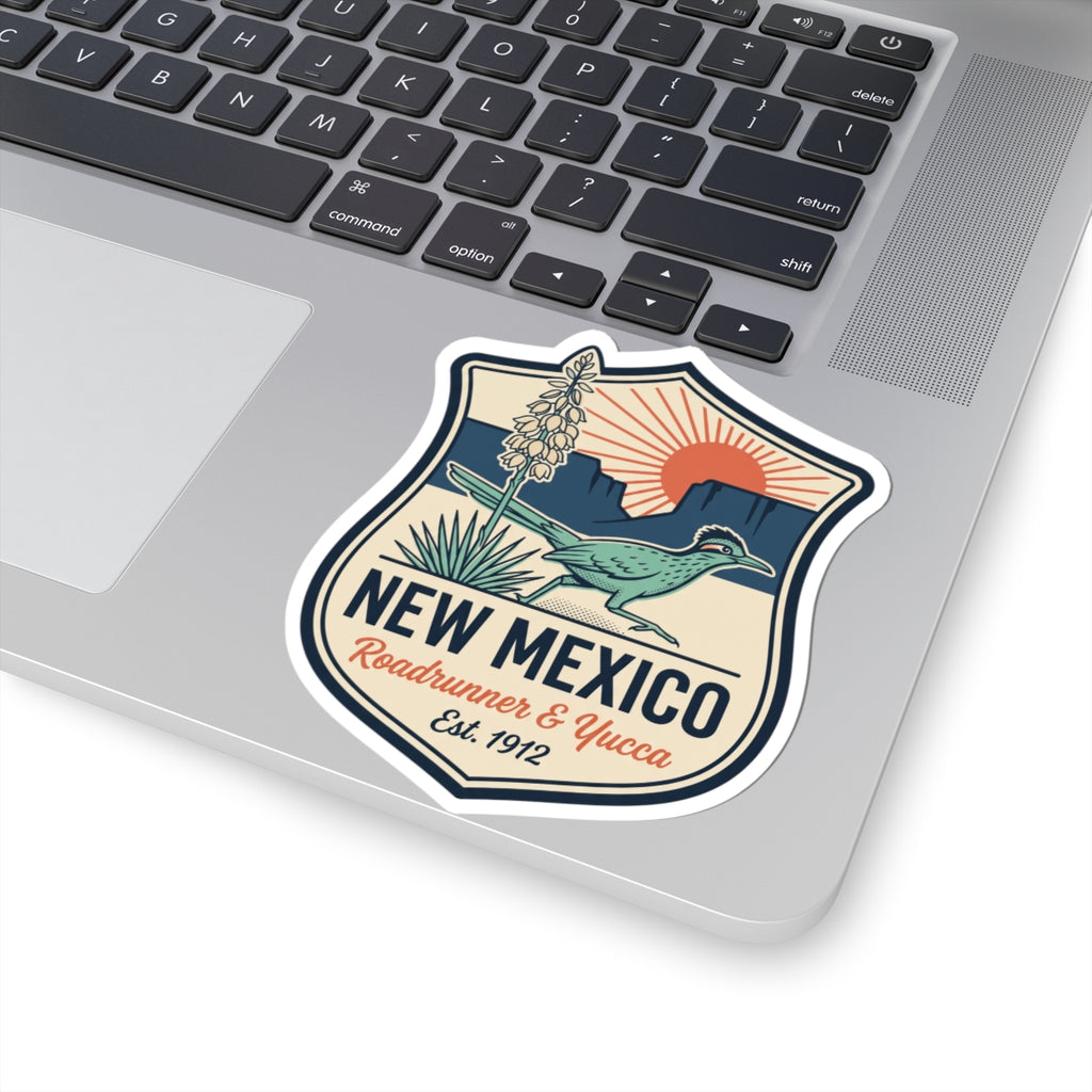 Shield-shaped vinyl sticker on a laptop lid with roadrunner, yucca, and “NEW MEXICO”