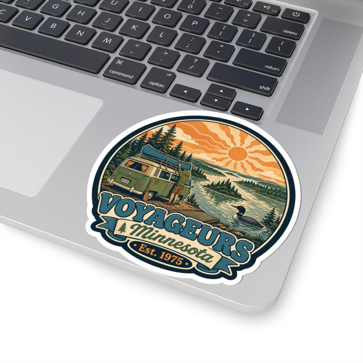 Round die-cut sticker featuring green camper van by lake, pine trees, orange sun; Voyageurs Minnesota