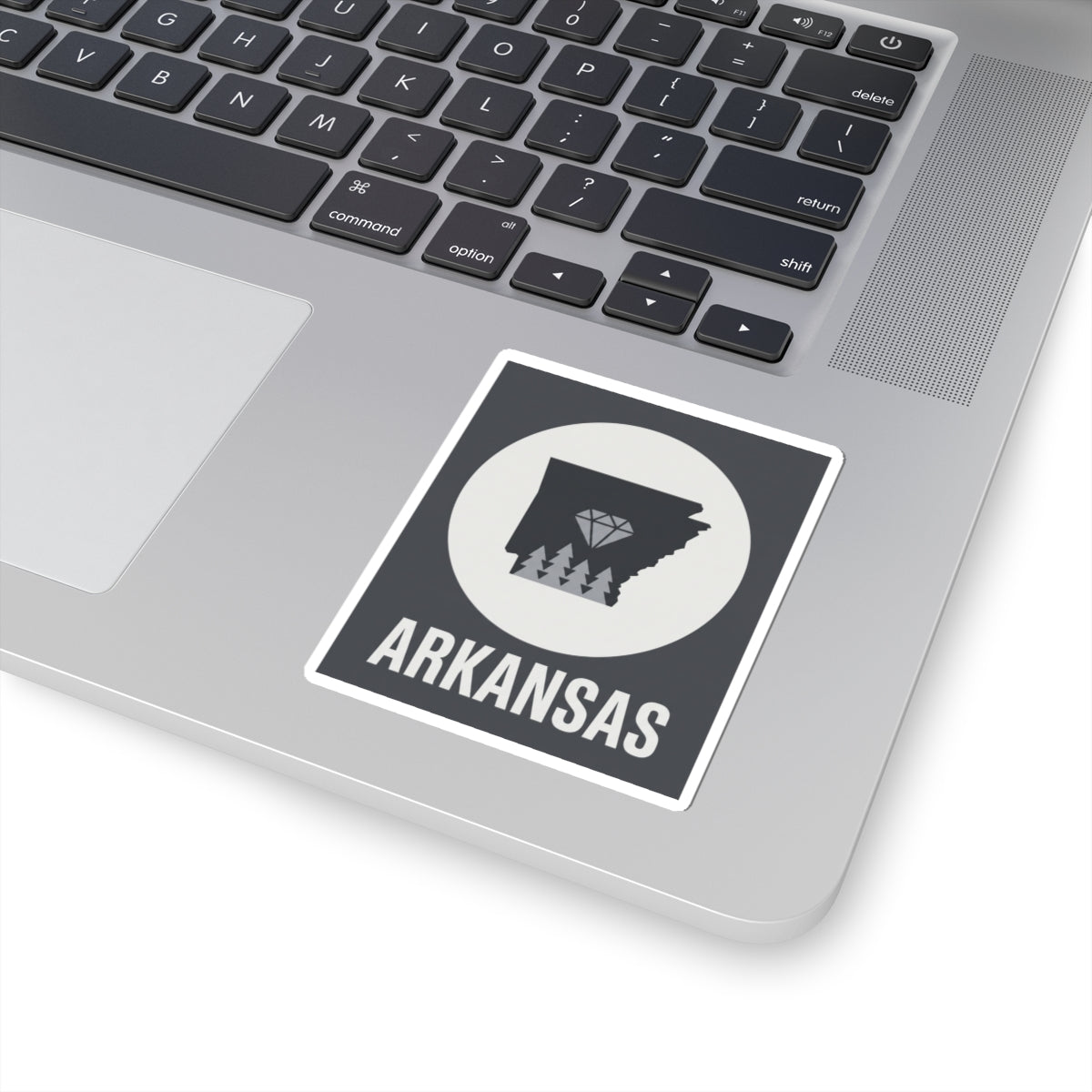 Arkansas vinyl sticker on laptop keyboard: dark state silhouette, diamond trees, ARKANSAS