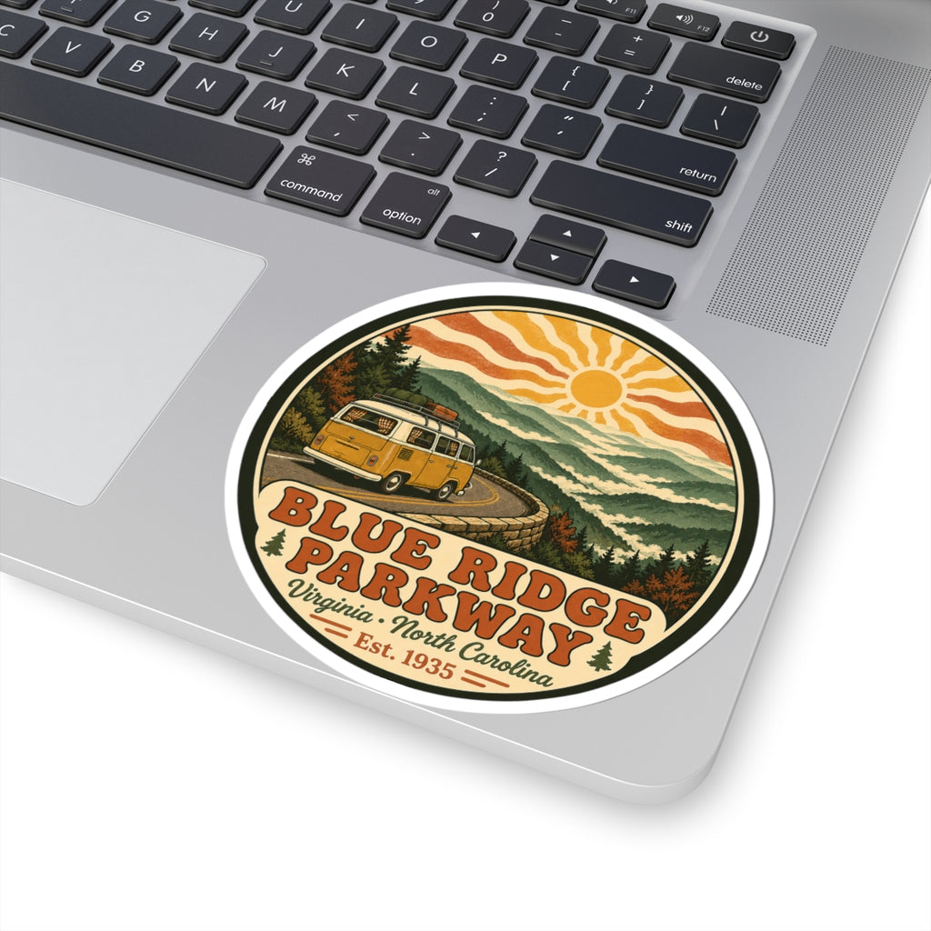 Circular sticker on laptop: yellow camper van on mountain road, sun and Blue Ridge Parkway lettering