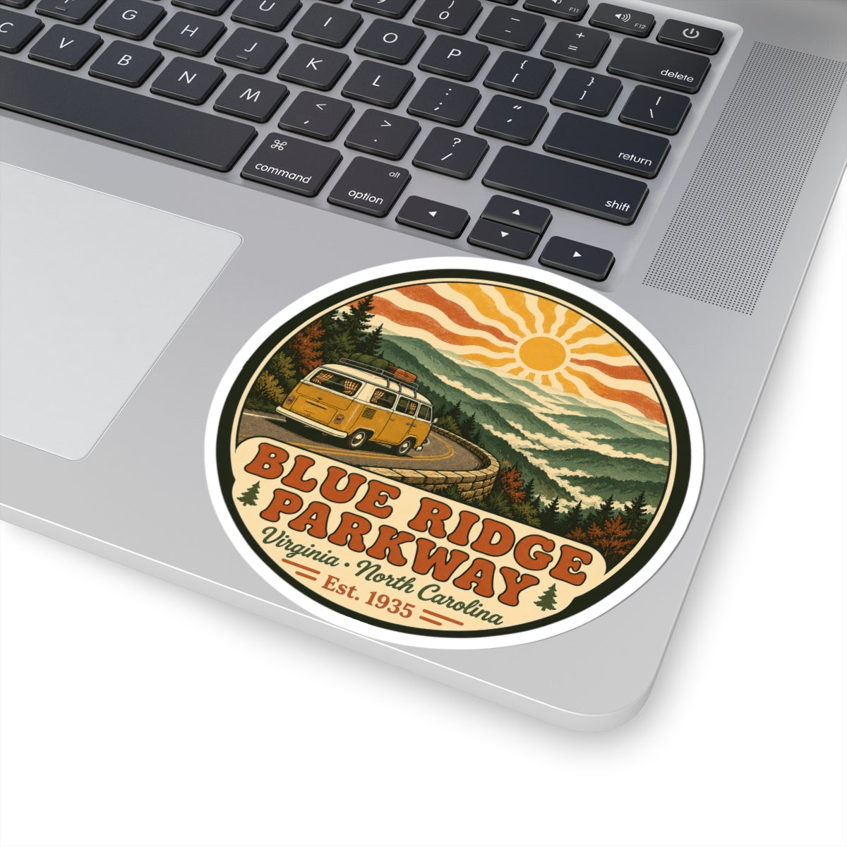 Circular sticker on laptop: yellow camper van on mountain road, sun and Blue Ridge Parkway lettering