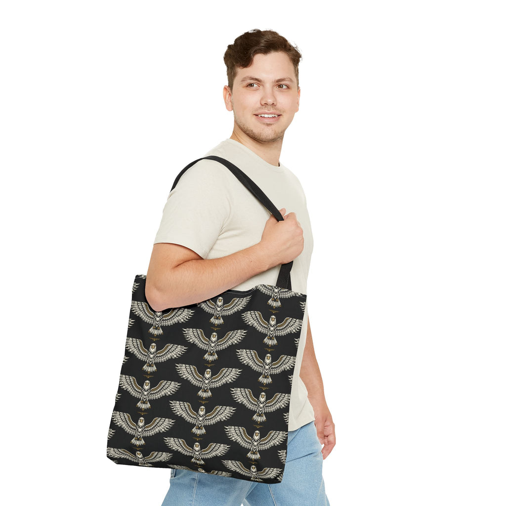 Black tote bag with gold winged scarab pattern, held at side with black strap