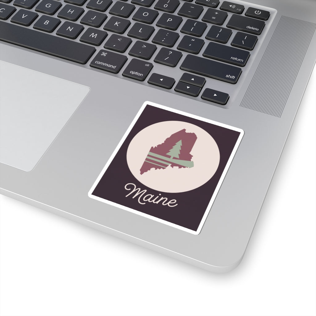 Maine silhouette vinyl decal on a laptop lid, mauve state with pine tree and 'Maine' script.