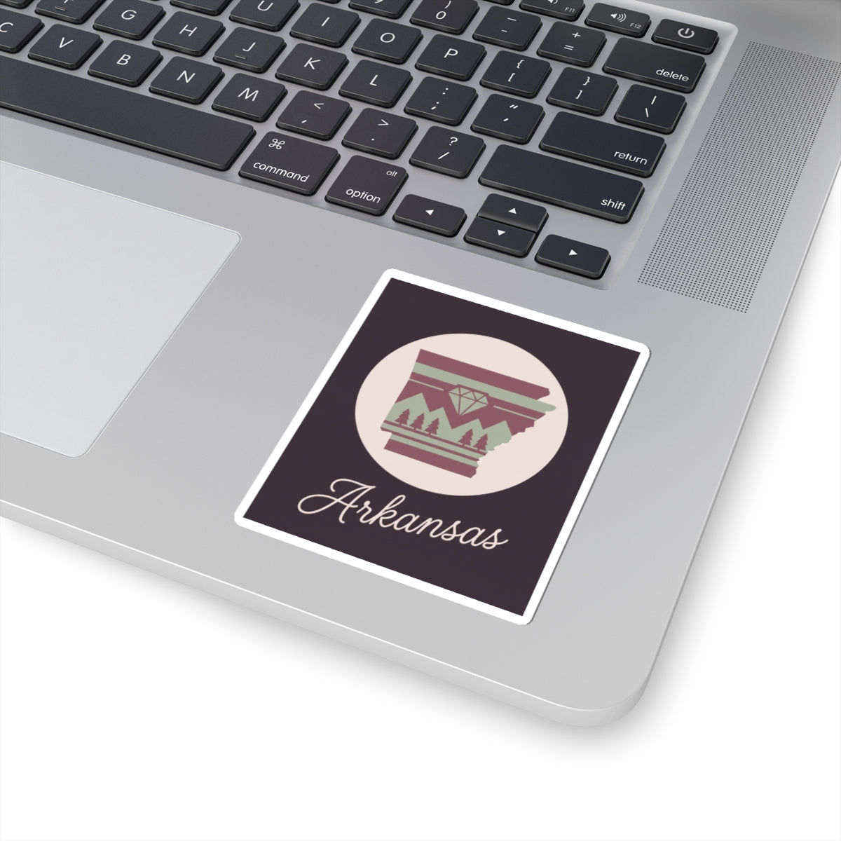 Arkansas state silhouette vinyl sticker on laptop keyboard, maroon and green circular emblem