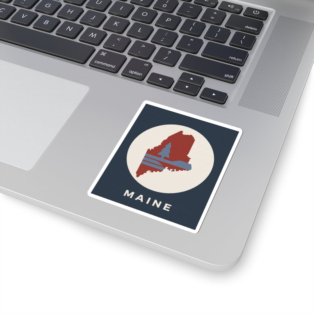 Maine state silhouette sticker on laptop: navy square with red map graphic and “MAINE”