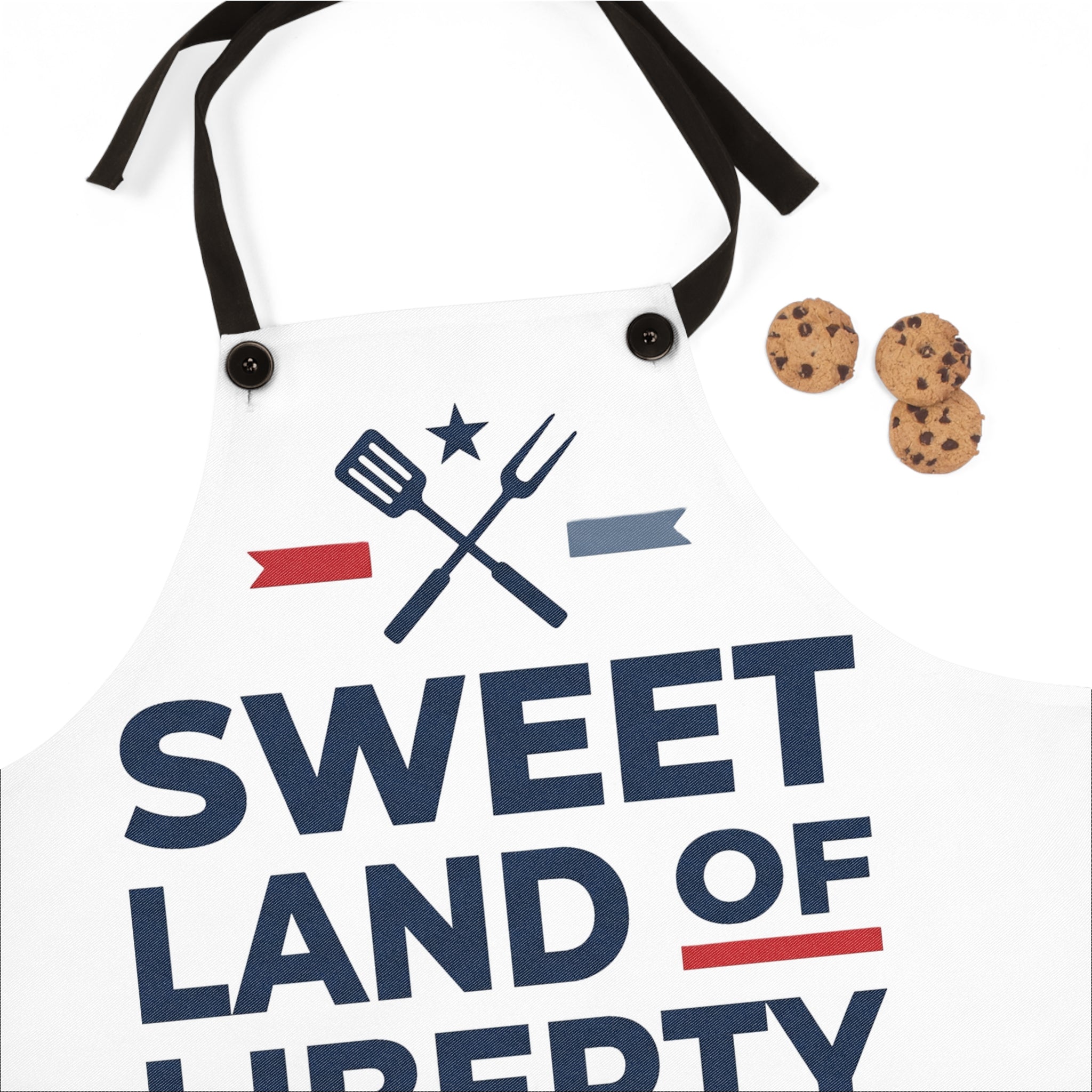 White BBQ apron close-up with crossed utensil graphic, black grommets, patriotic text