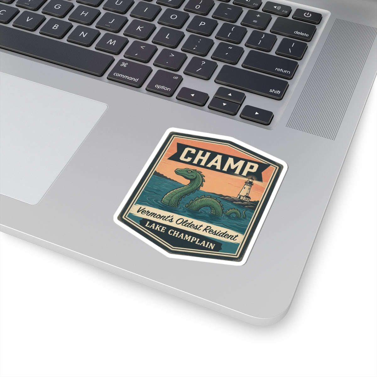 CHAMP themed sticker on a laptop trackpad, with green sea serpent and lighthouse artwork