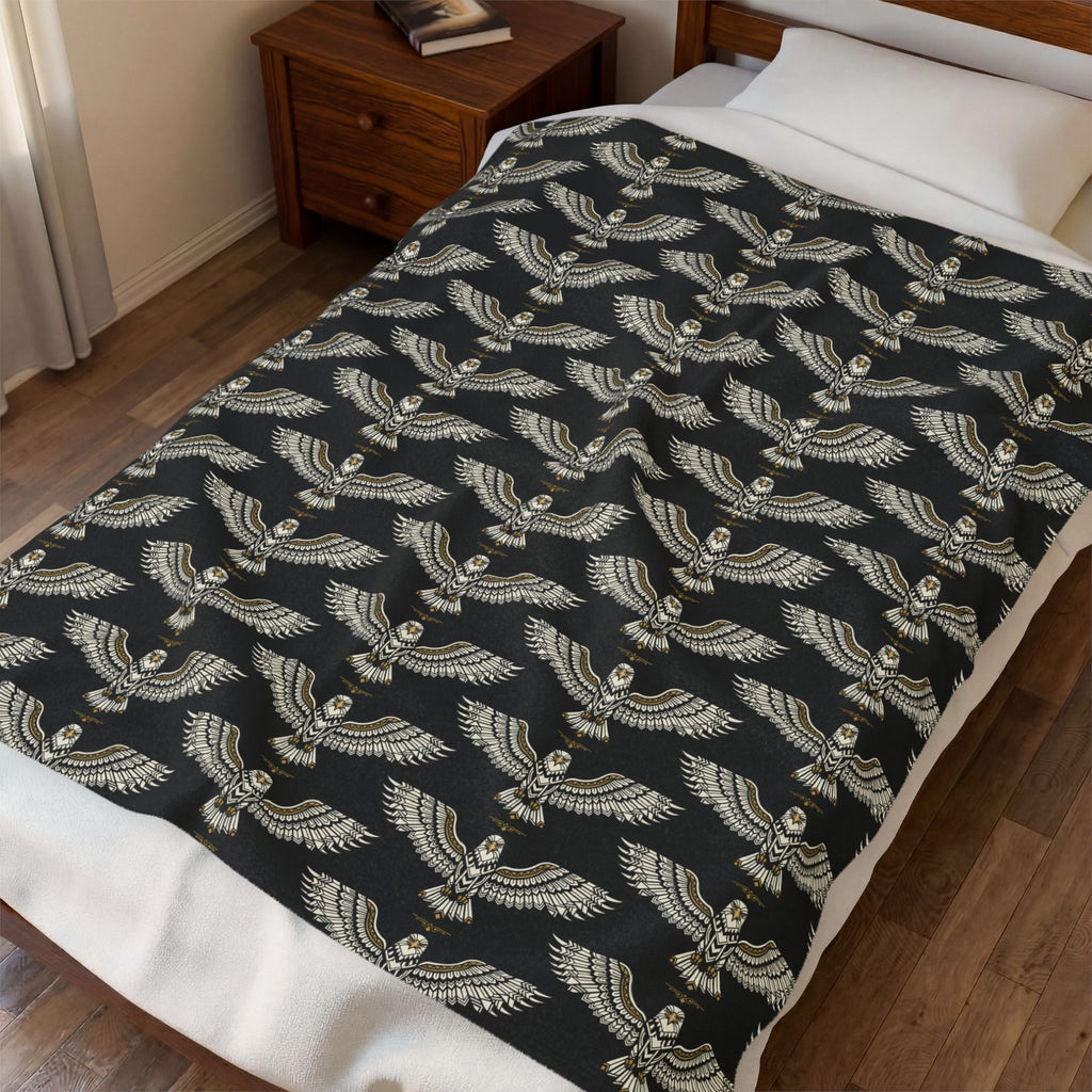Velveteen plush blanket on bed with winged skull pattern in gold on dark background