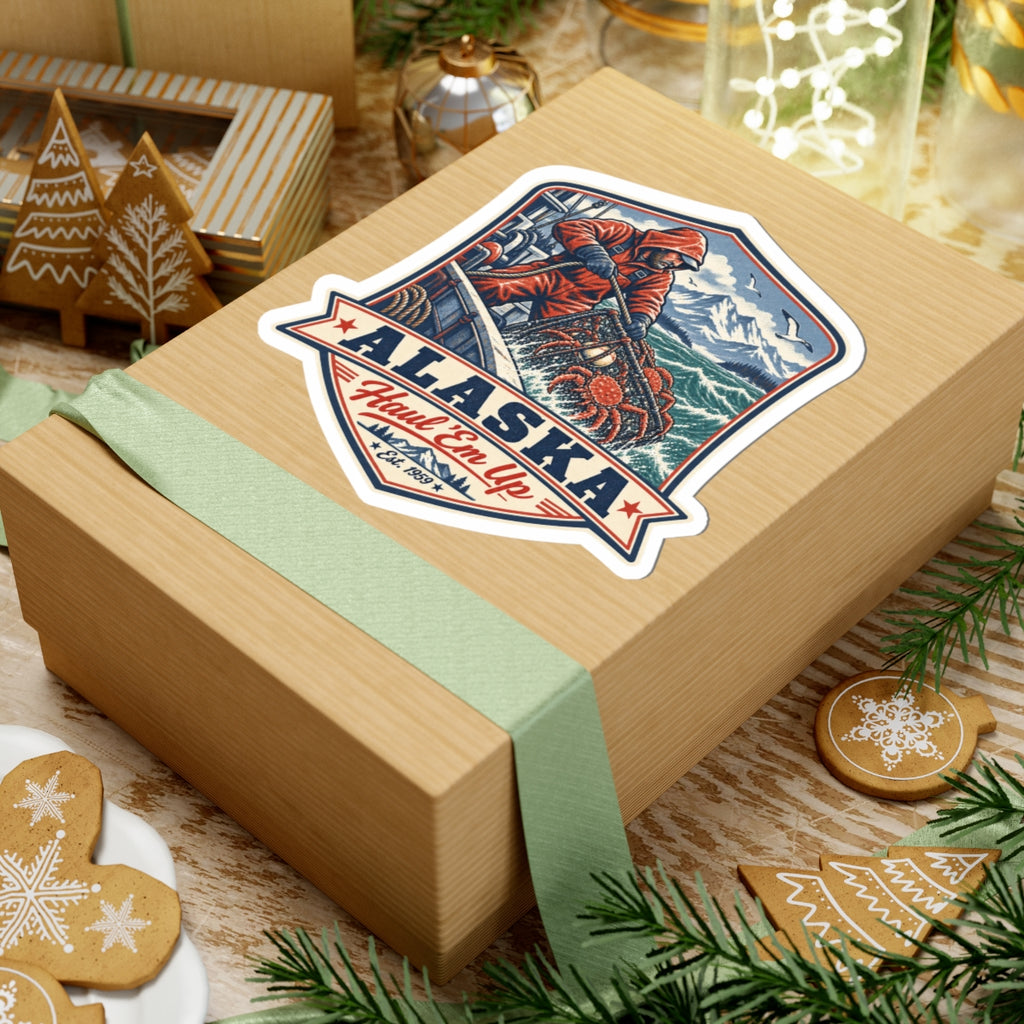 Alaska fisherman crab sticker on a gift box, featuring orange coat, crab pot, and red "ALASKA"