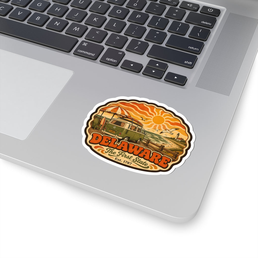 Delaware oval sticker placed on laptop keyboard; vintage van and orange sun beach artwork