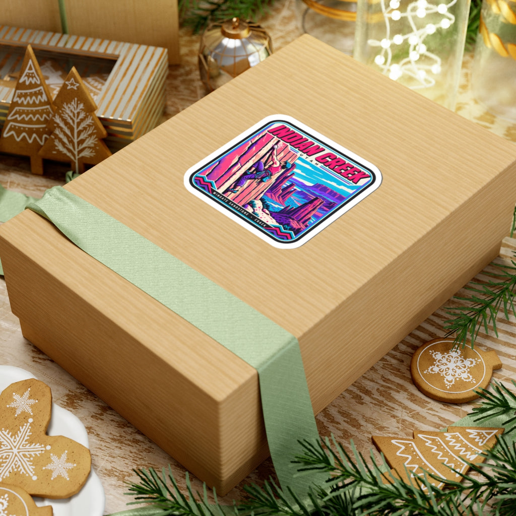 Square “INDIAN CREEK” sticker on a gift box lid with green ribbon and desert climber art