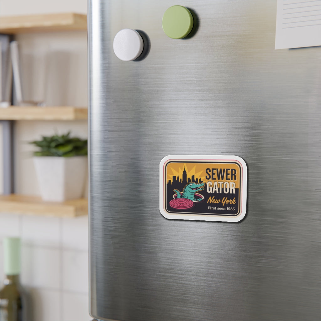 Die-cut refrigerator magnet on brushed stainless fridge, small Sewer Gator New York emblem.