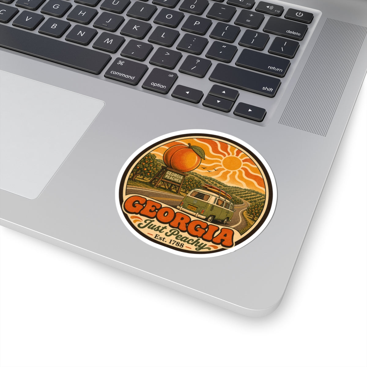Round vinyl sticker on white laptop lid, with Georgia Just Peachy orange peaches and green van