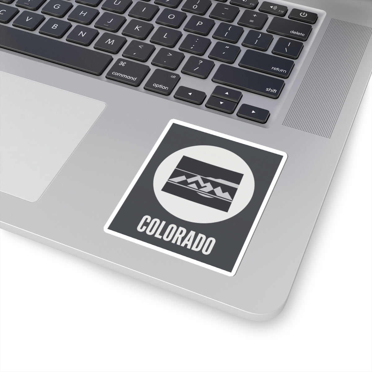 Colorado badge sticker placed on a dark square with white border, mountain emblem, and COLORADO