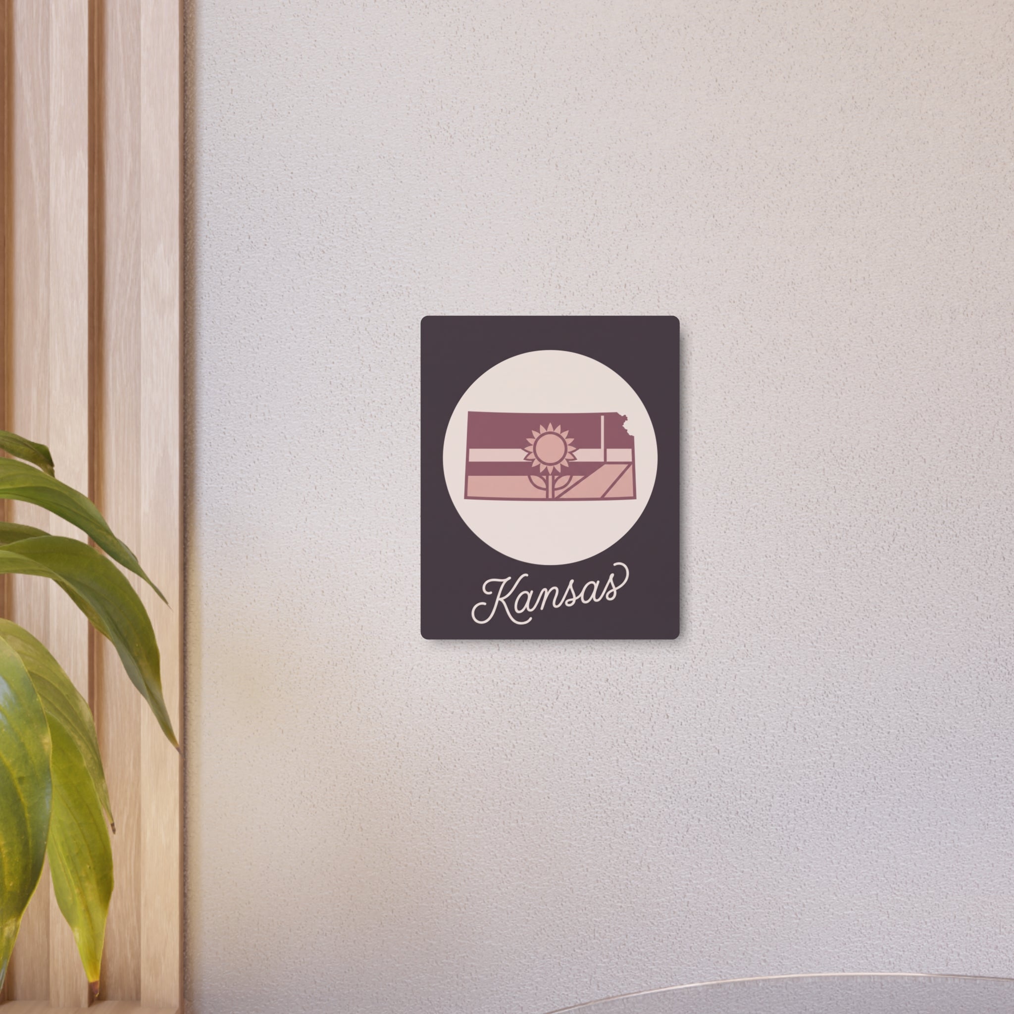 Kansas metal wall art sign mounted on wall: dark square panel with oval sun landscape and Kansas.