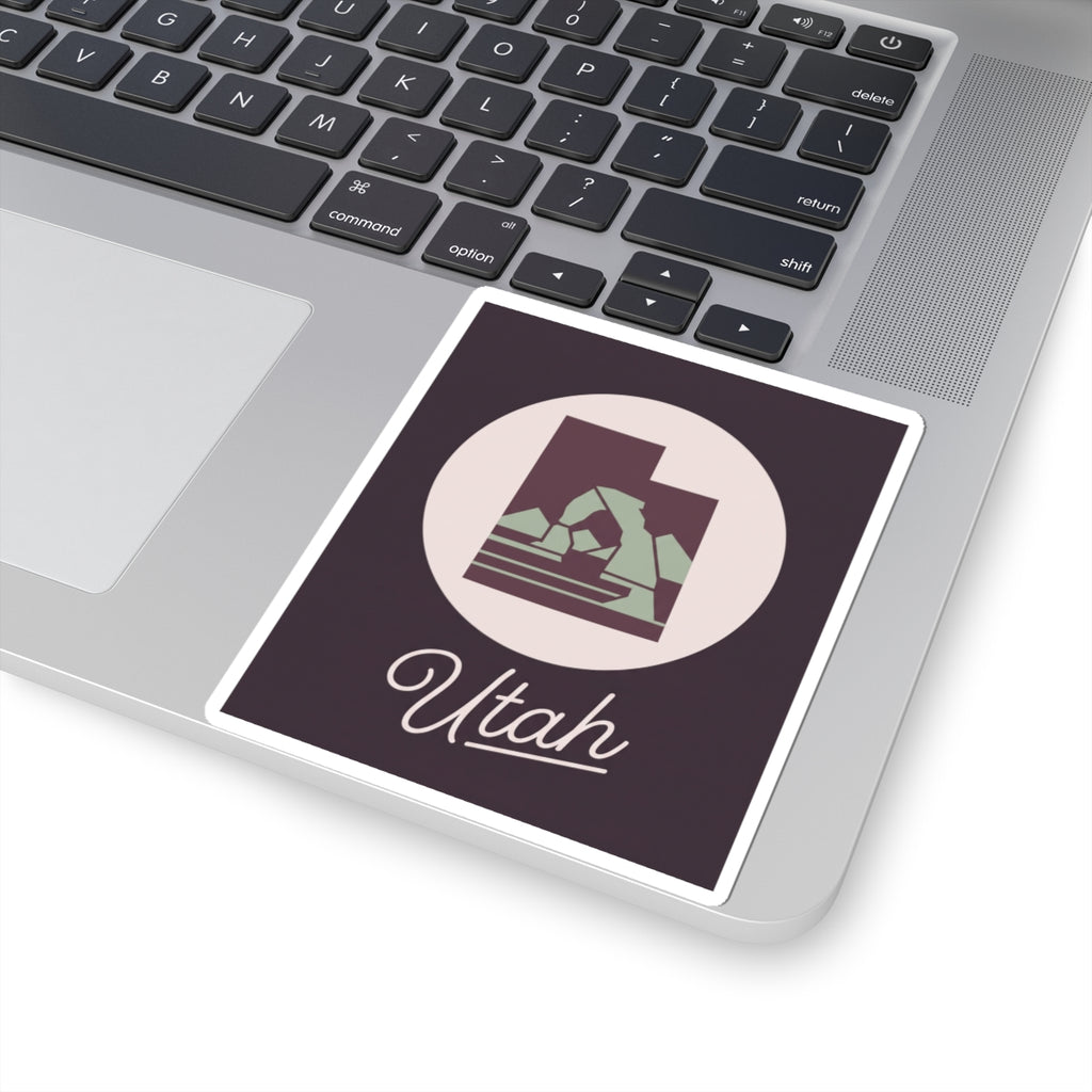 Utah state decal sticker on a laptop surface, dark purple square with circular mountain and “Utah”.