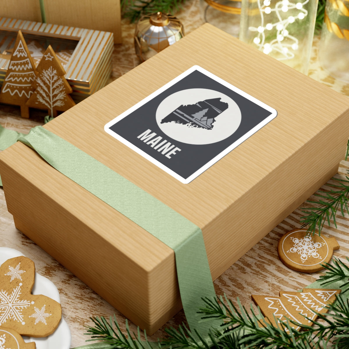 Maine silhouette sticker on gift box: dark rectangle with circular pine tree map and 'MAINE'.