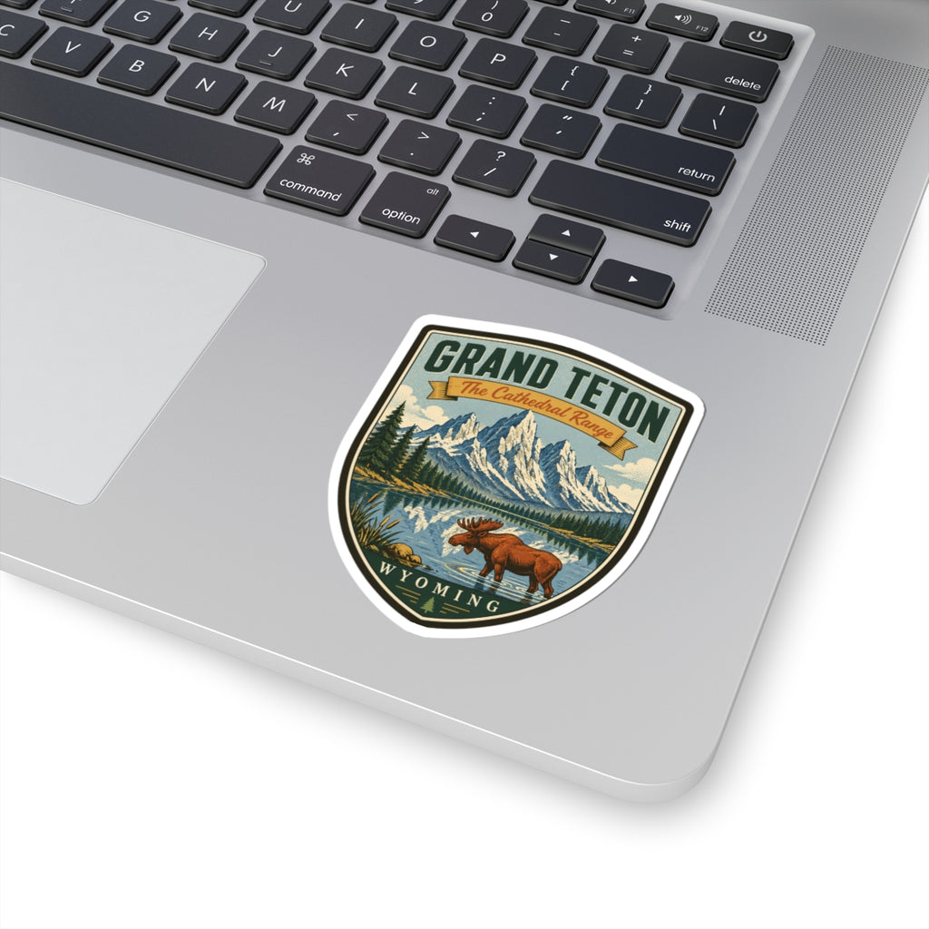 Shield-shaped travel sticker on a laptop keyboard, showing moose, mountains, lake, and Wyoming text.