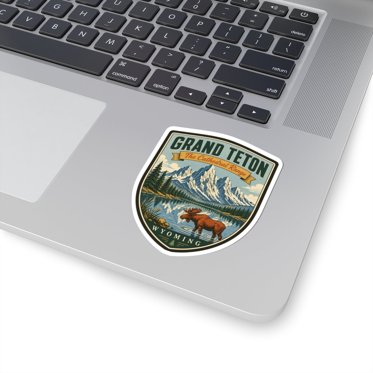 Shield-shaped travel sticker on a laptop keyboard, showing moose, mountains, lake, and Wyoming text.