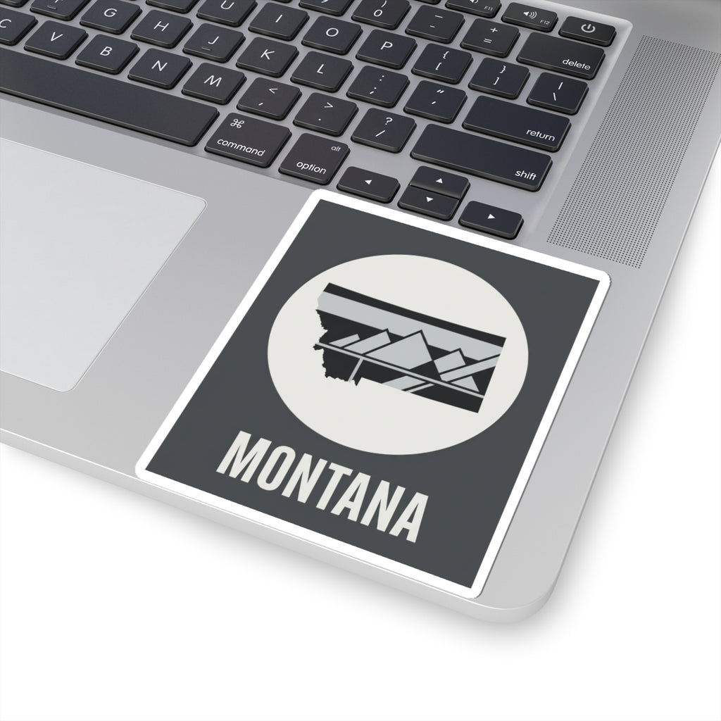 Montana mountain badge sticker on laptop screen, white circle emblem with landscape graphic and MONTANA